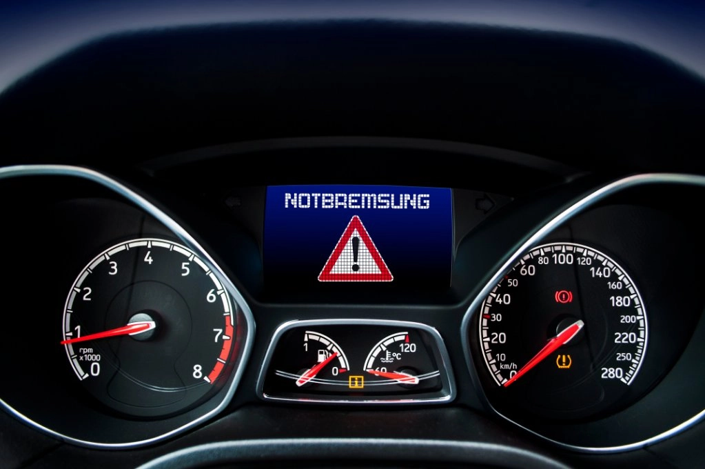 Cockpit mit Warnanzeige „Notbremsung“ und rotem Warndreieck im Display