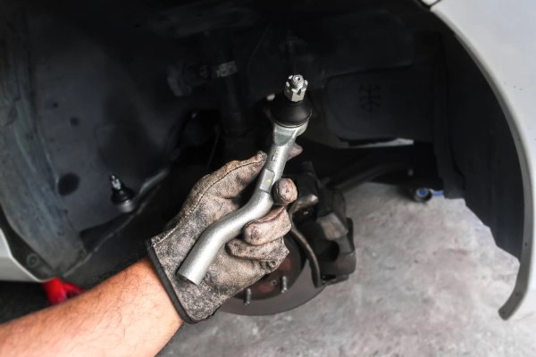 Eine Hand mit Handschuh hält eine Spurstange in der Hand