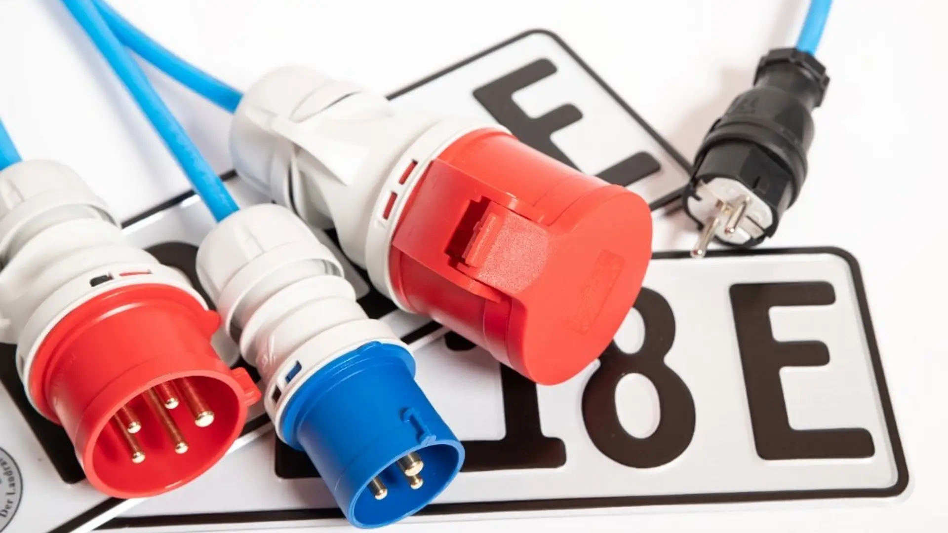 Ladestecker für Elektroautos liegen auf einem Kennzeichen mit „E“ für Elektrofahrzeug