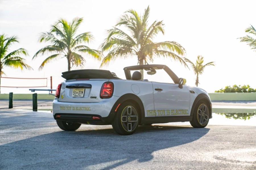 Weißer Mini Cooper steht angewinkelt mit dem Heck während im Hintergrund Palmen und Sonne zu sehen sind