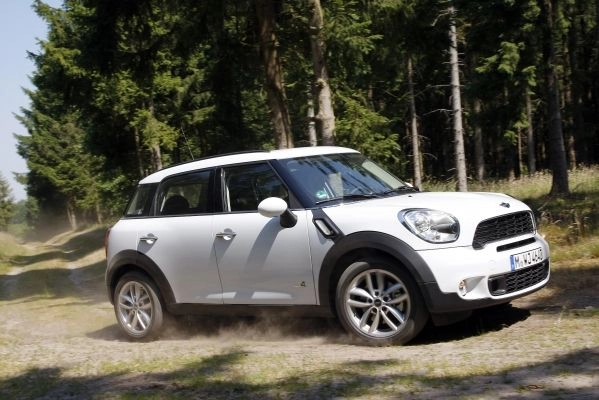 Weißer MINI Countryman fährt auf einem Waldweg, im Hintergrund sind Bäume zu sehen