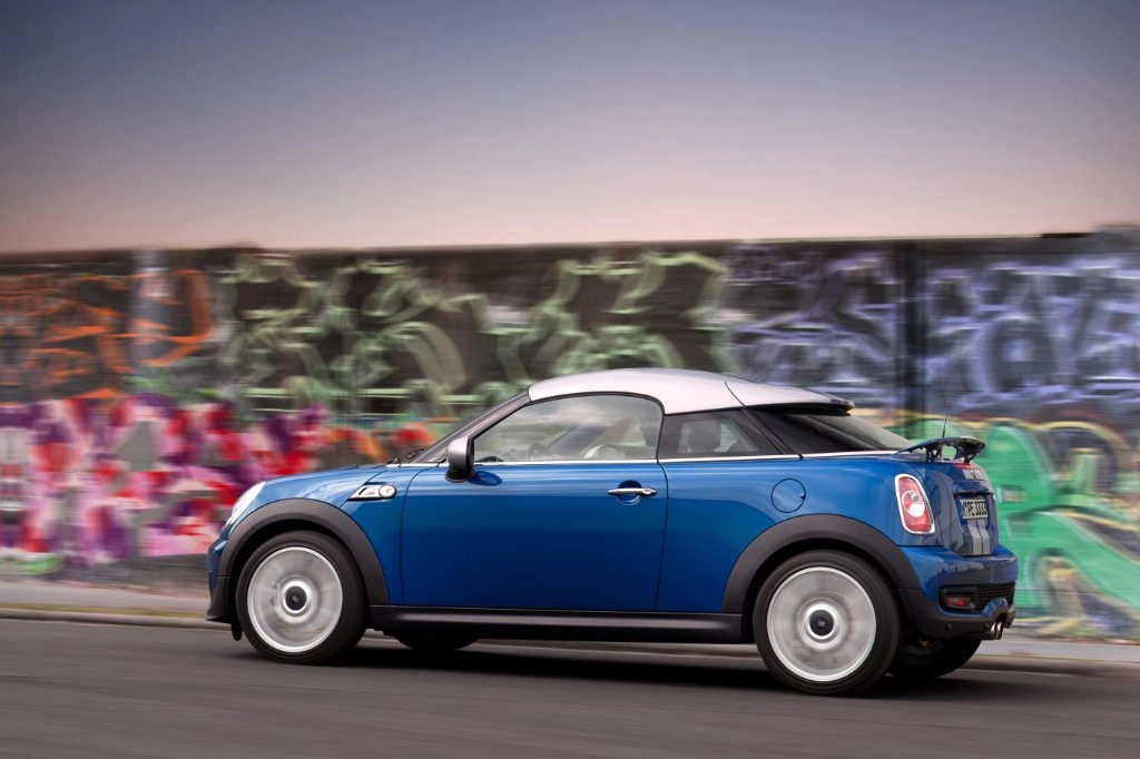 Blauer MINI Coupé fährt an einer Graffiti-Wand vorbei