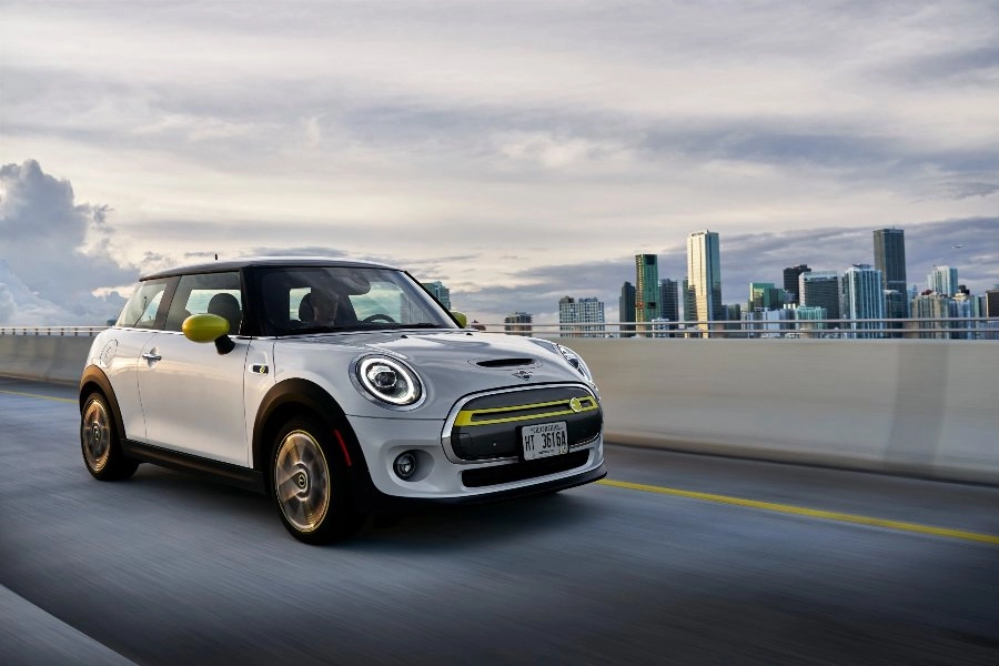Weißer MINI Cooper fährt auf einer Straße, im Hintergrund ist eine moderne Skyline mit Hochhäusern zu sehen
