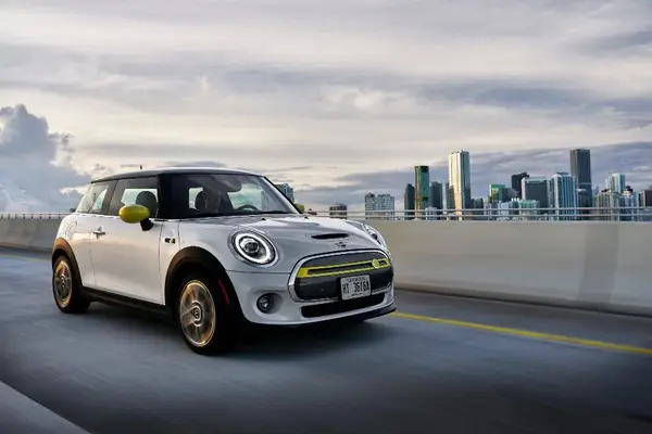 Weißer MINI Cooper fährt auf einer Straße, im Hintergrund ist eine moderne Skyline mit Hochhäusern zu sehen