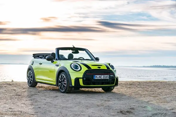 Neongelber Mini Cooper steht am Strand bei Sonnenuntergang