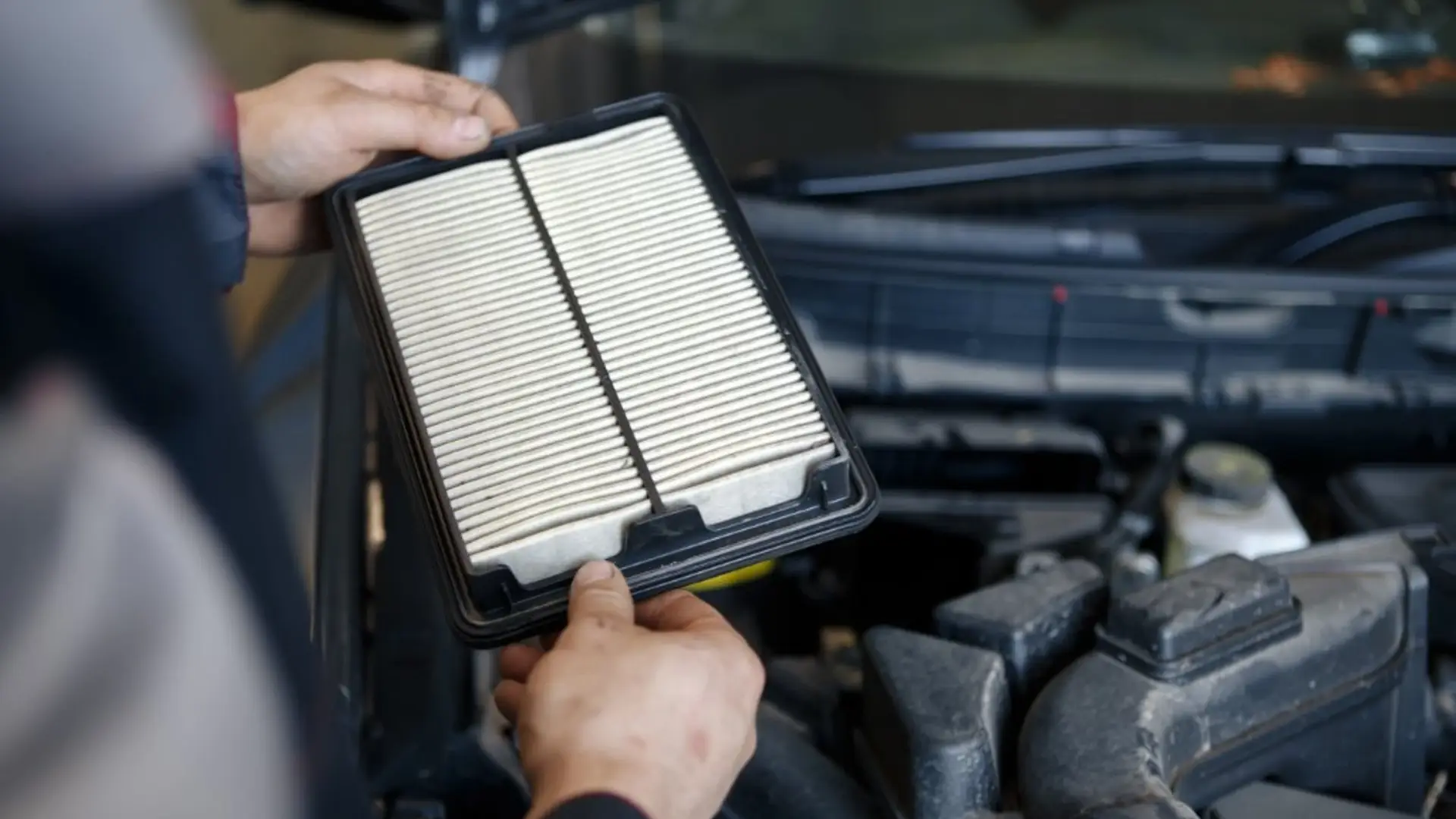 Person hält einen Motor-Luftfilter im Motorraum eines Fahrzeugs