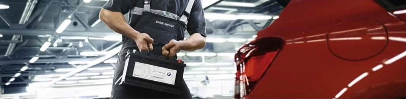 Ein Mann trägt eine Autobatterie neben einem roten BMW in einer Werkstatt