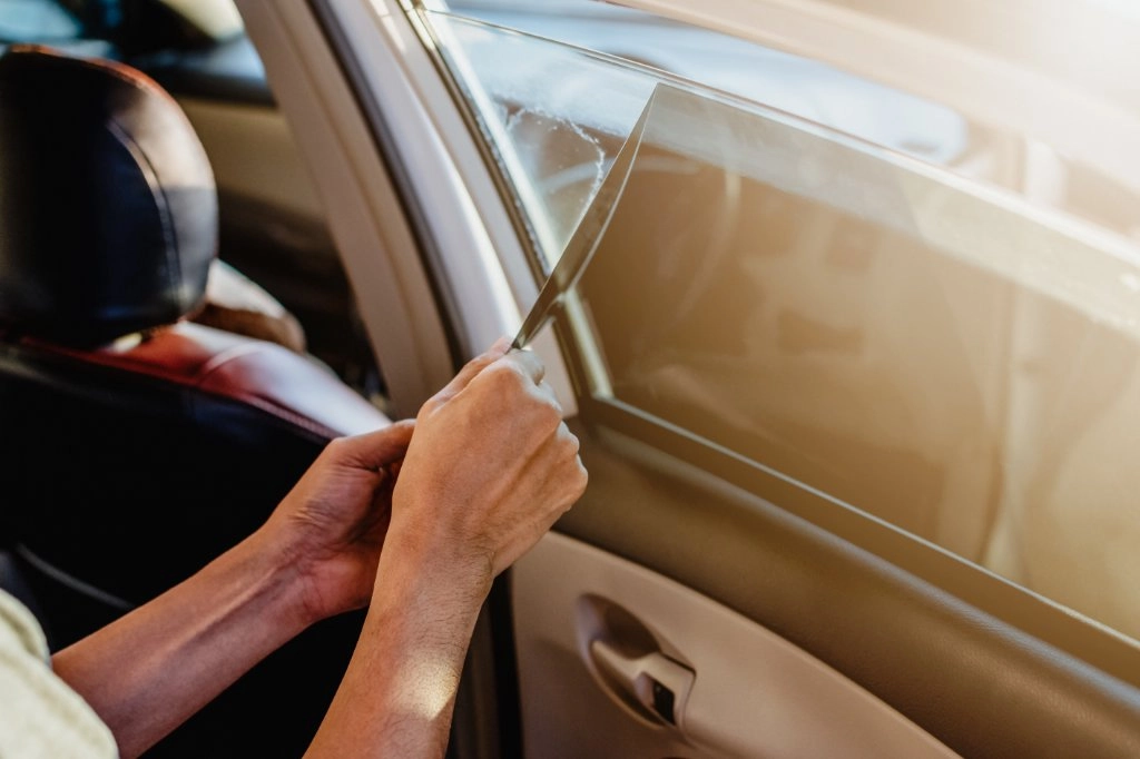 Person entfernt Scheibentönungsfolie von einer Autoscheibe