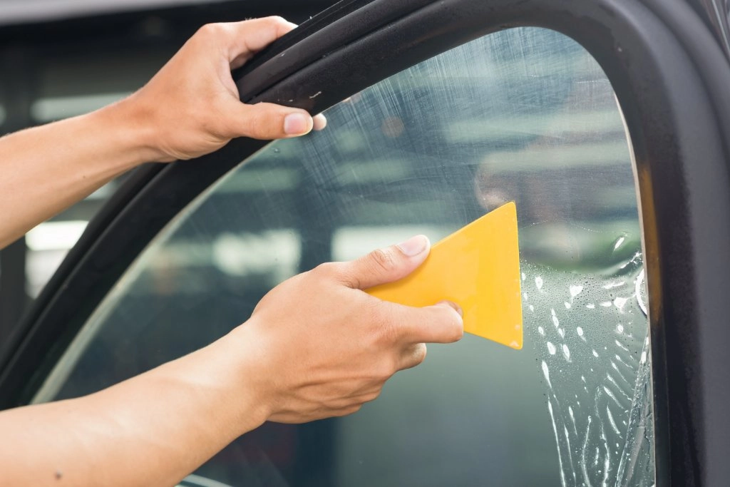 Person befestigt Scheibentönungsfolie an einer Autoscheibe mit einem Rakel