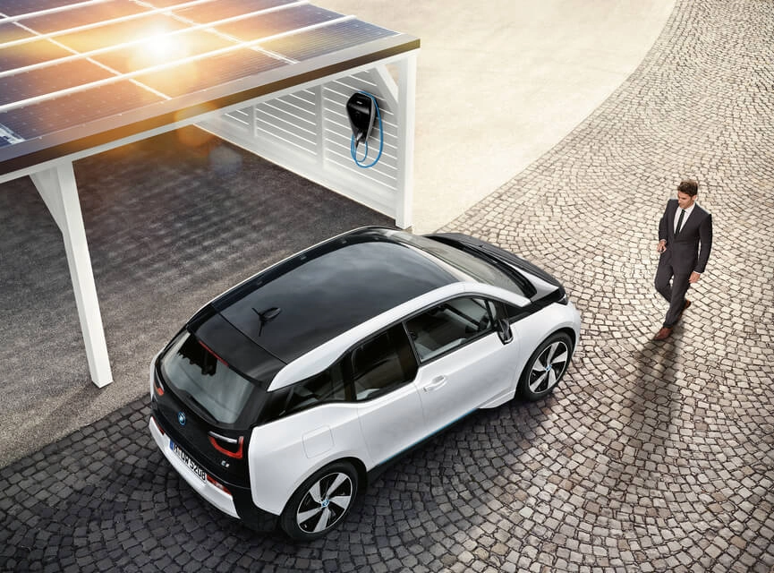 BMW i3 steht unter einem Carport mit Solardach und Ladestation, daneben steht ein Mann auf gepflastertem Boden