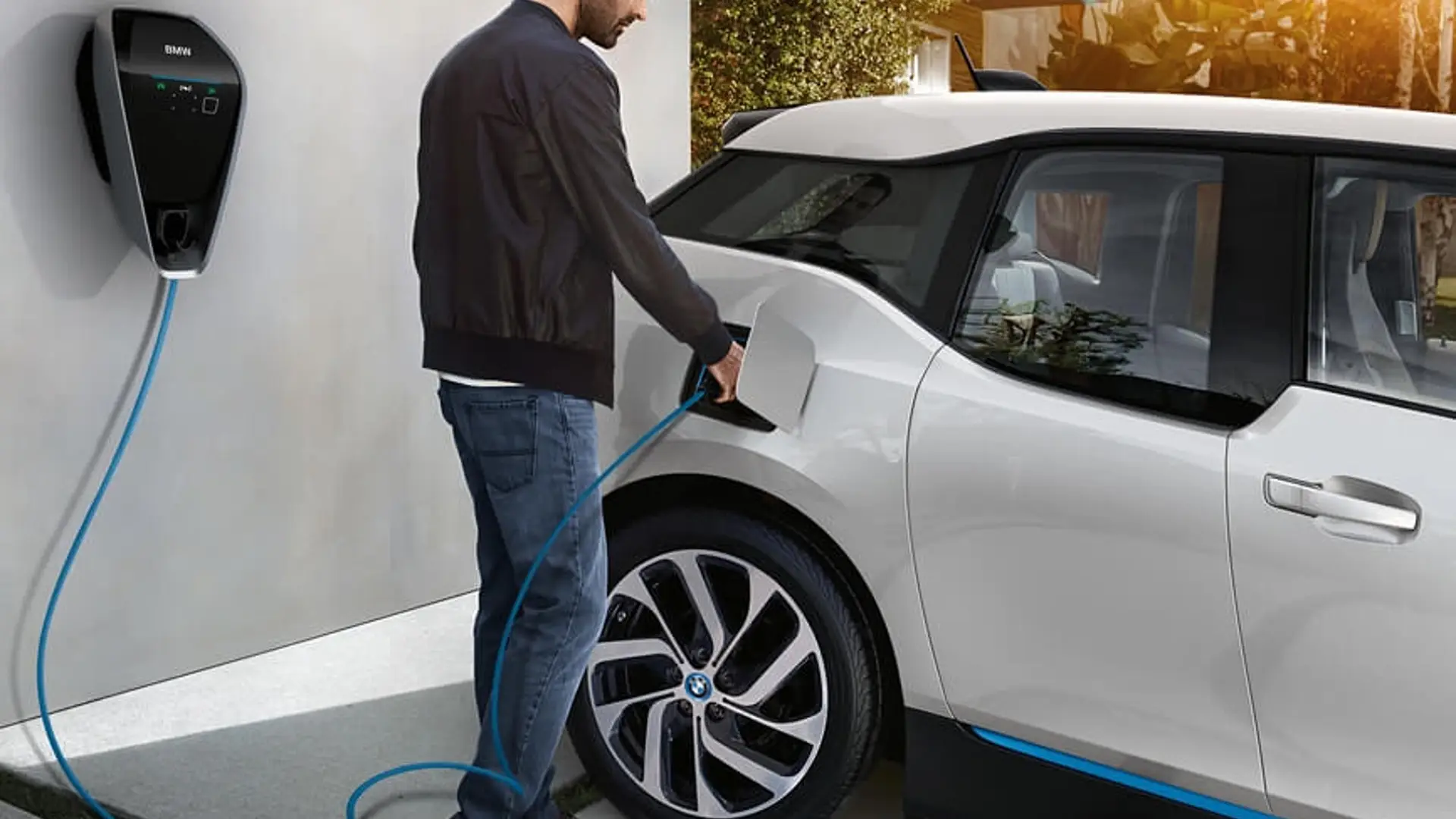 Ein Mann lädt einen BMW i3 an einer Wandladestation, das Ladekabel ist am Fahrzeug angeschlossen