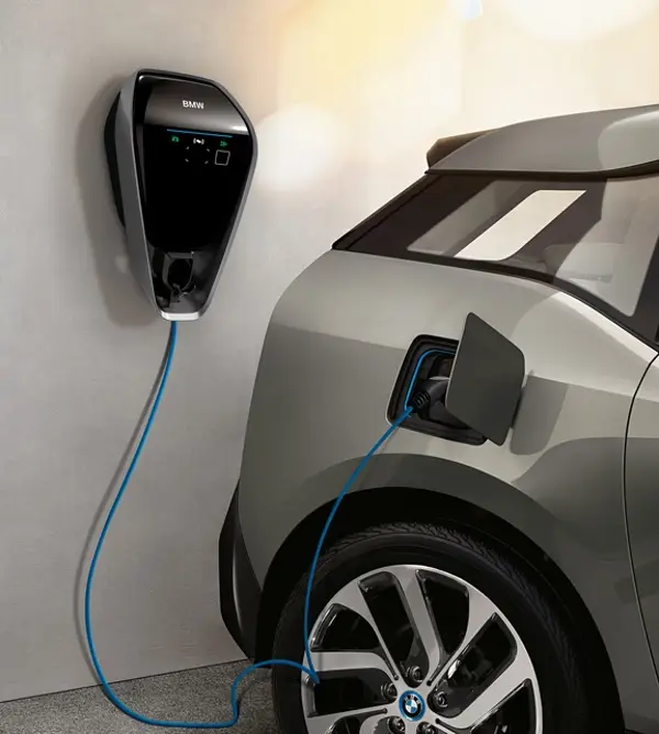 BMW i3 ist an einer Wallbox-Ladestation angeschlossen, das Ladekabel führt von der Wand zum geöffneten Ladeanschluss am Fahrzeug