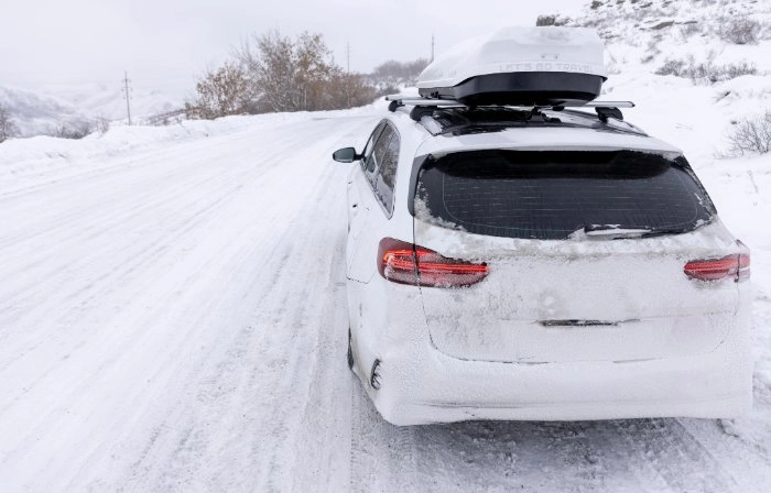 Auto mit Dachbox fährt durch eine Schneelandschaft